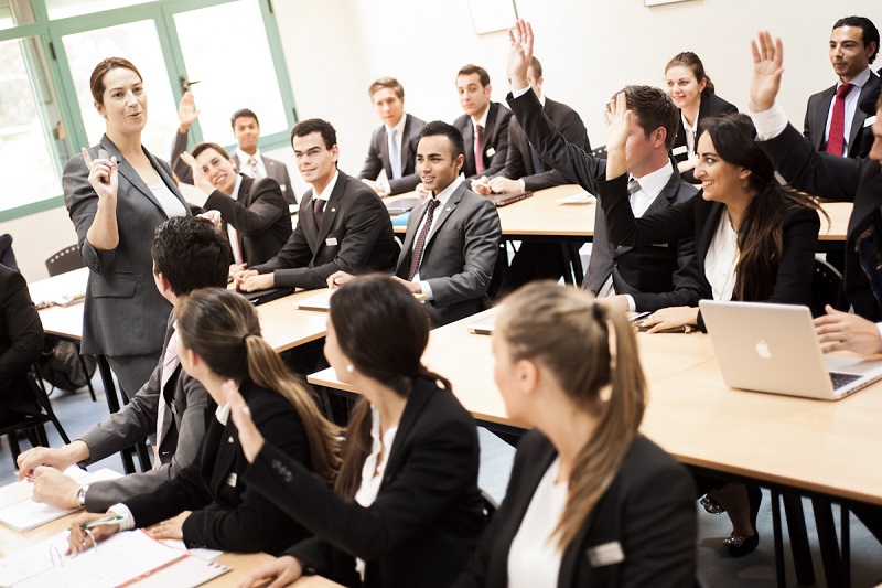 Portrait of business people in business school raising hands in training session
